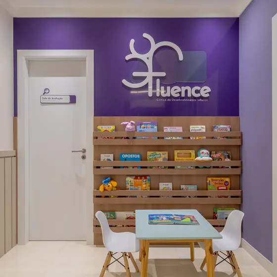 Espera da Clínica Fluence, com o letreiro branco sobre a parede roxa.